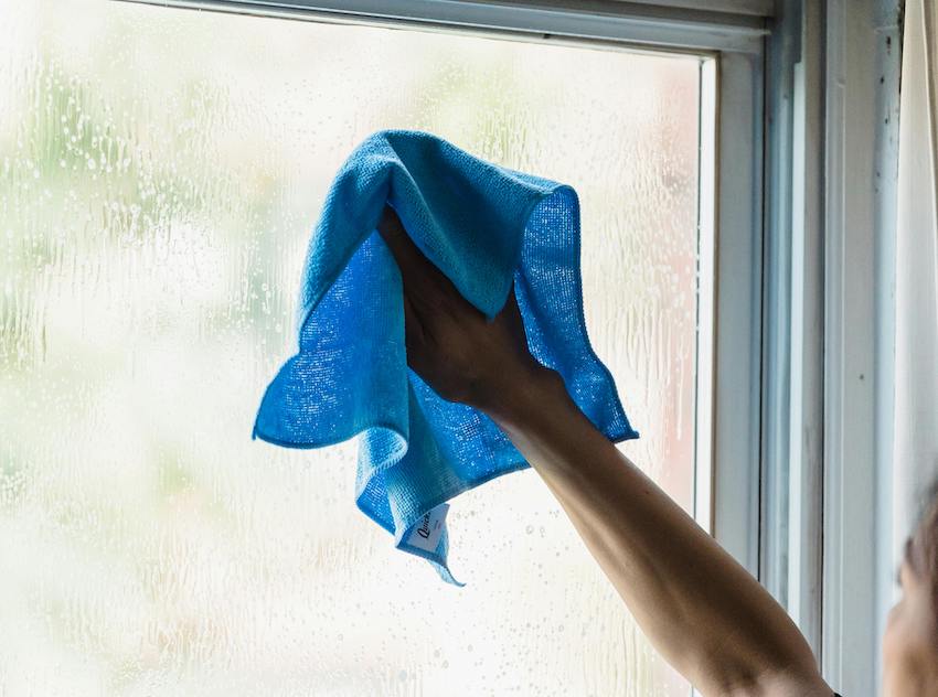 Benefits of Hiring a Professional House Cleaner. Cleaning window with blue fiber cloth.
